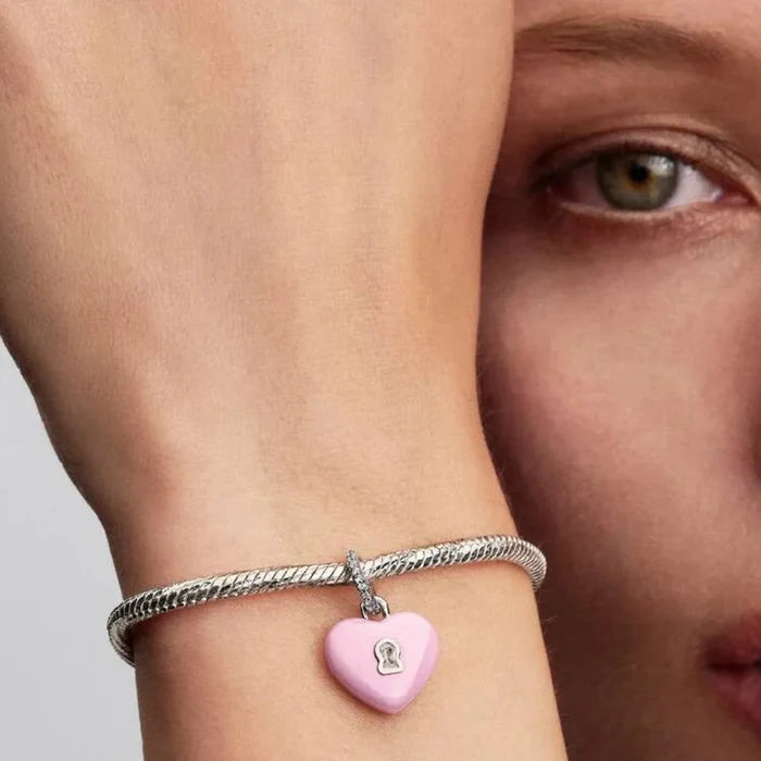 Close-up of a wrist wearing a silver bracelet with a pink heart charm, against a neutral background.