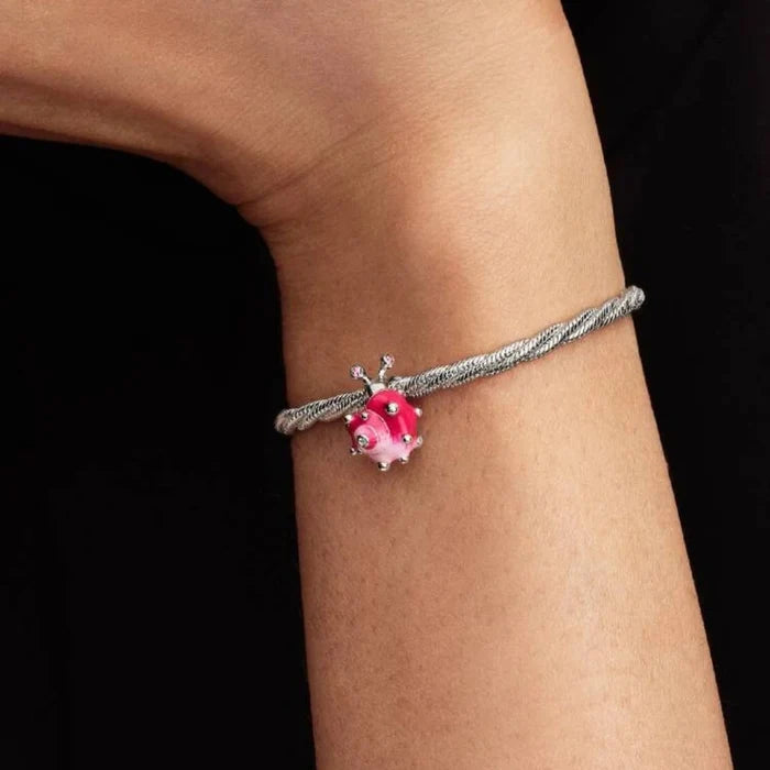 Silver bracelet with a pink charm on a wrist against a black background
