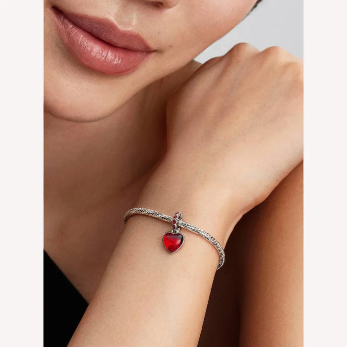 Close-up of a woman's wrist wearing a bracelet with a red heart charm.