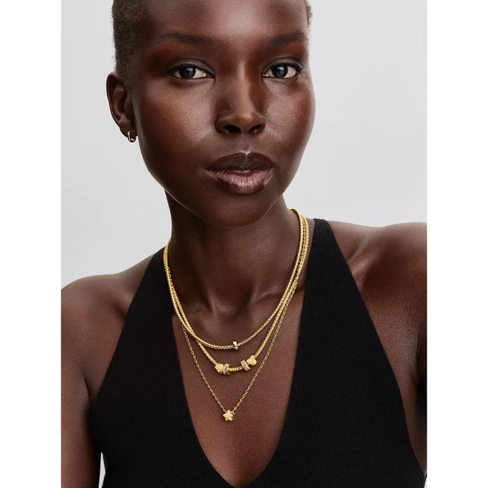 Woman wearing layered gold necklaces, including the Pandora Ribbed Clip Charm styled as a pendant, paired with other charms.