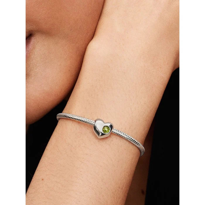 Woman wearing a Pandora bracelet with the Spring Green Stone Heart Charm in sterling silver and green crystal.