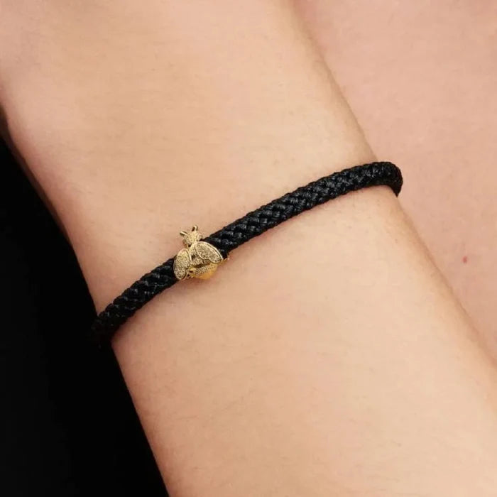 Black braided bracelet with a gold charm on a wrist against a neutral background