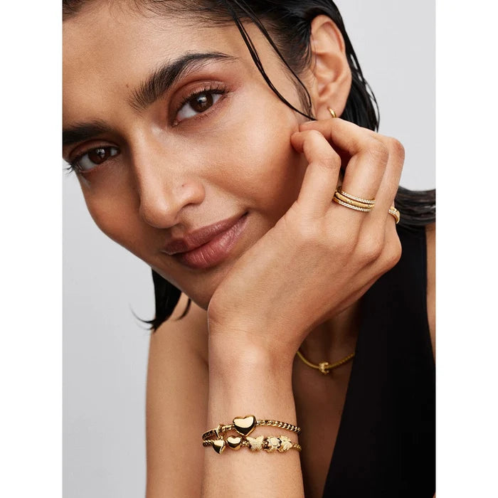 A woman wearing layered gold jewelry including rings, bracelets, and a necklace featuring the four-leaf clover charm.
