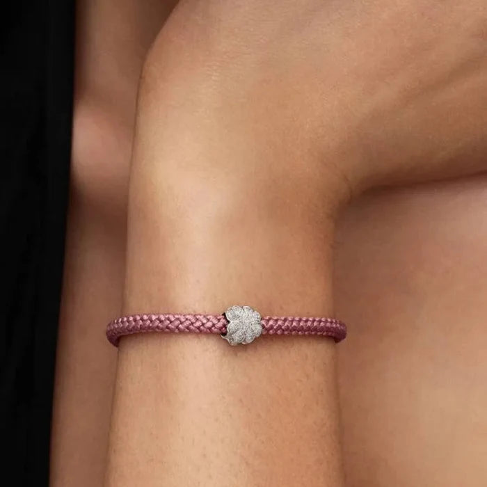 Pink braided bracelet with a  clover on a wrist against a neutral background