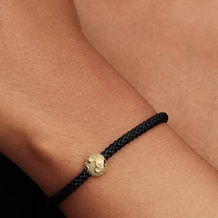 Black braided bracelet with a gold globe charm on a wrist.