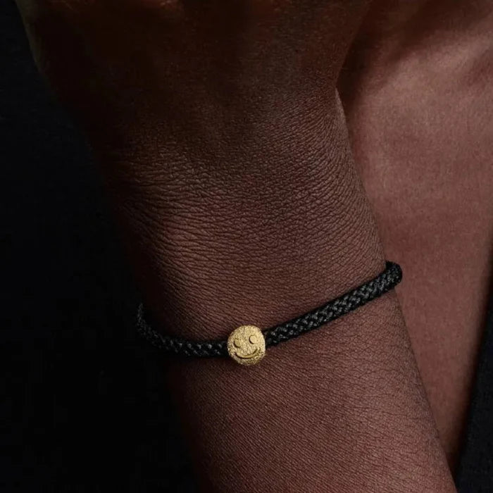 Black braided bracelet with a gold charm on a wrist against a dark background