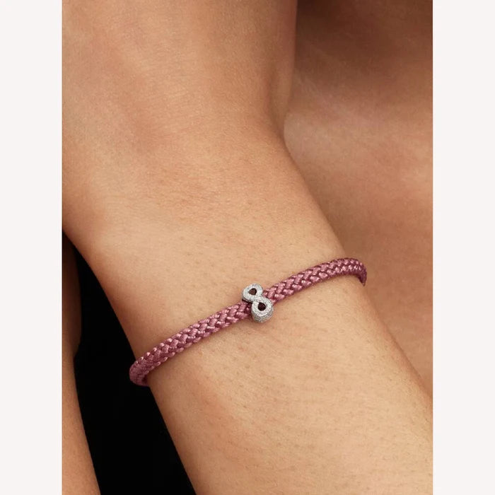 Pink braided bracelet with a silver charm on a wrist