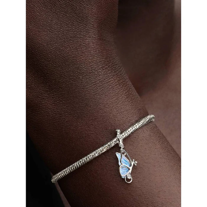 Pandora Winged Dangle Charm styled on wrist, showing silver butterfly with shimmering blue enamel wings.