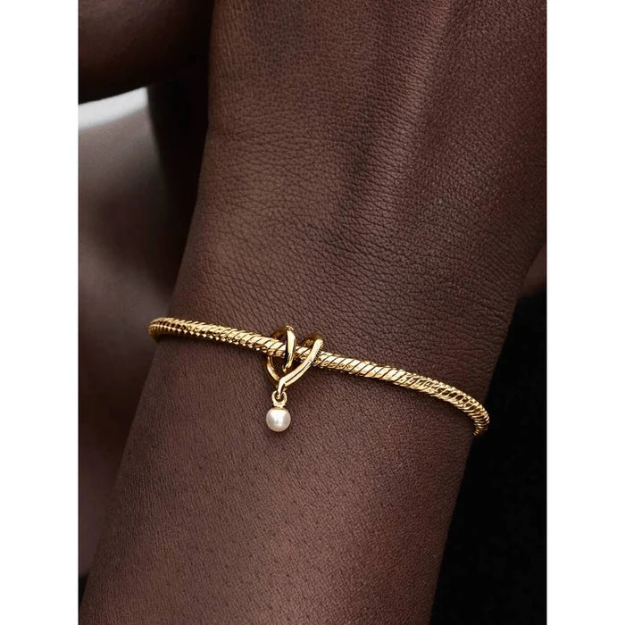 Close-up of a person wearing a gold Pandora snake chain bracelet with the Wrapped Heart Charm featuring a dangling pearl.