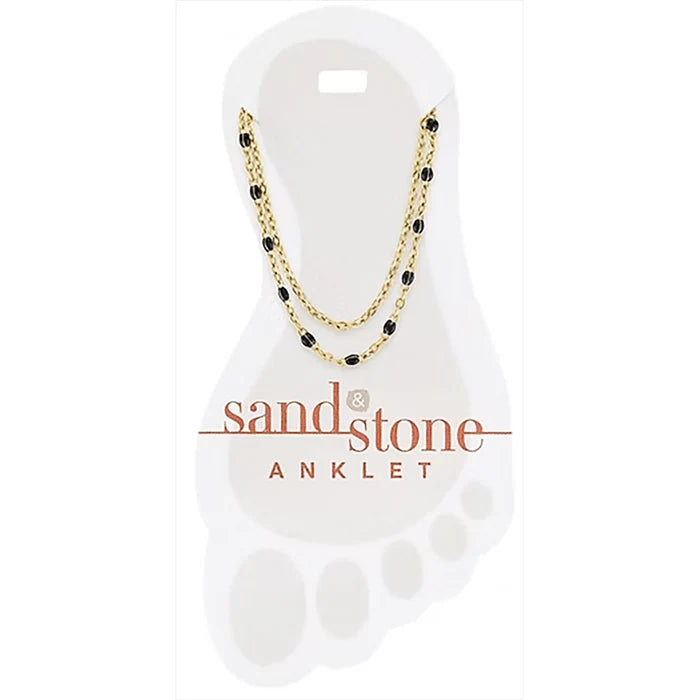 Gold and black beaded anklet on a 'sand & stone' branded card.