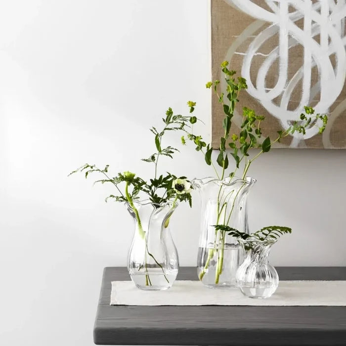A clear glass vase characterized by a flowing wavy design, emphasizing its stylish and contemporary appearance.