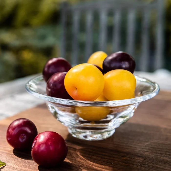 A colorful bowl of assorted fruit, including apples, bananas, and oranges, placed on a wooden table.
