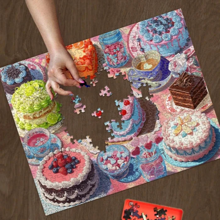 Puzzle with colorful cake illustrations on a wooden surface, featuring a hand placing a piece.