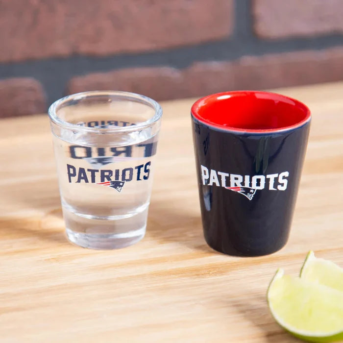 Two shot glasses with 'Patriots' branding on a wooden surface.