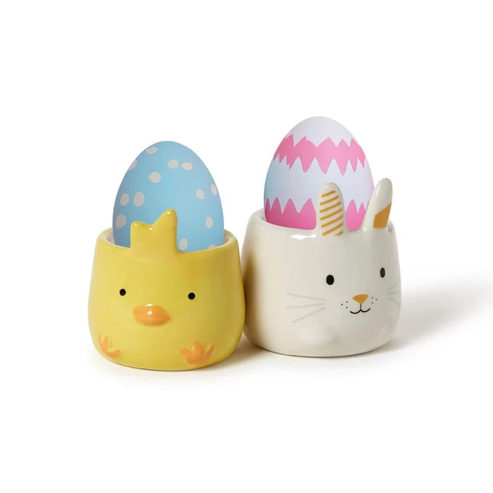 Two ceramic eggs, one containing a bunny and the other a chick, are displayed together in a decorative arrangement.