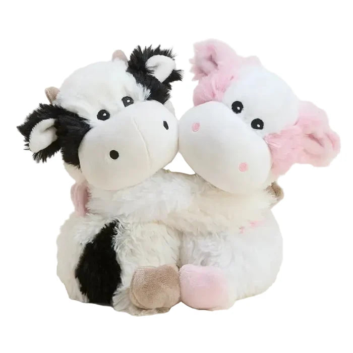 Two cute plush cow toys hugging, one with a black and white pattern and the other with pink accents, set against a plain light beige background.