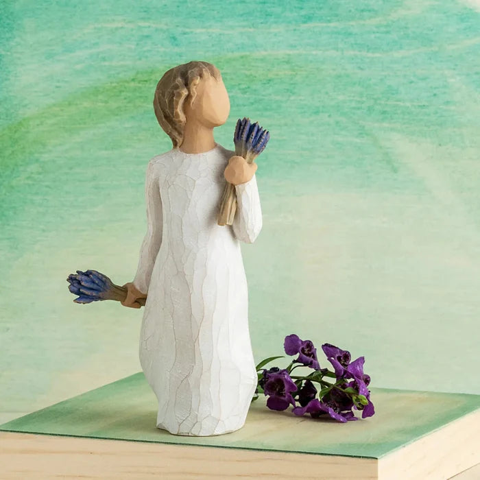 Figurine of a person holding purple flowers against a green and blue gradient background