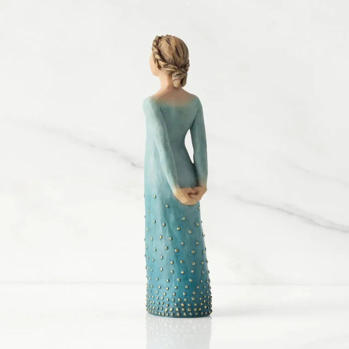 Statue of a woman wearing a long, light blue dress with gold embellishments on a white background