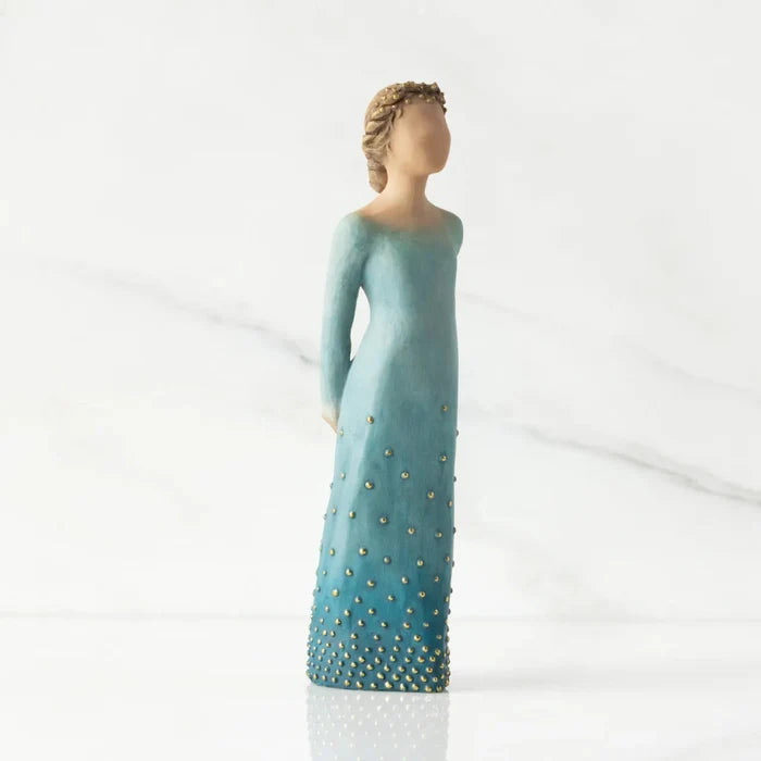 Statue of a woman in a long, light blue dress with gold embellishments on a white background