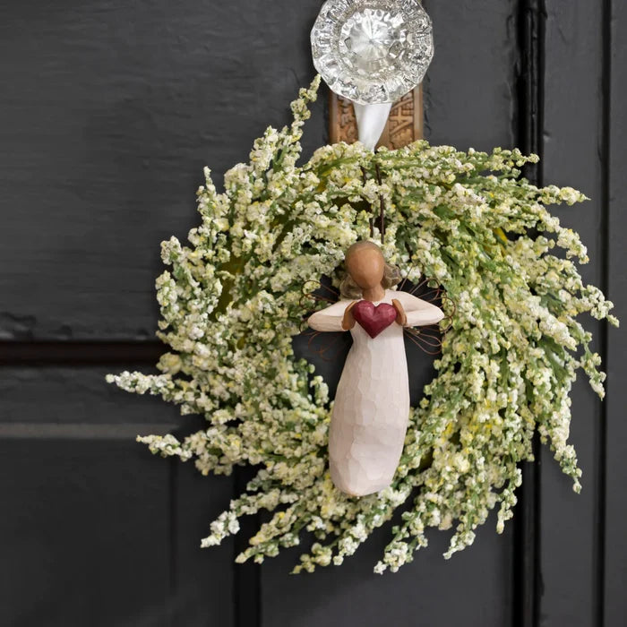 Decorative wreath with an angel figure holding a heart on a black door.