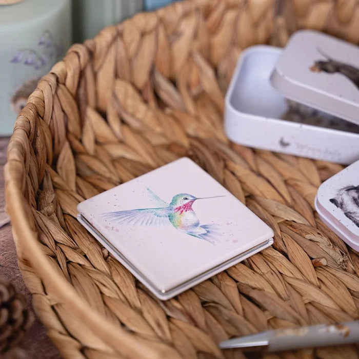 Wrendale Designs Hummingbird Compact Mirror displayed in a wicker basket, featuring colorful hummingbird illustration.