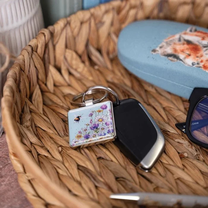 A square keychain adorned with a bee and vibrant flowers, showcasing a cheerful design.