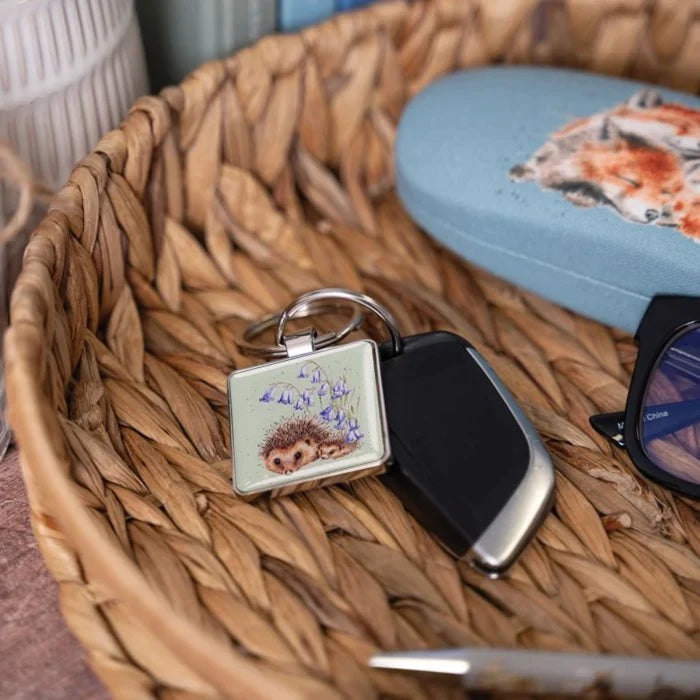 A square keychain showcasing a hedgehog nestled among vibrant bluebells.