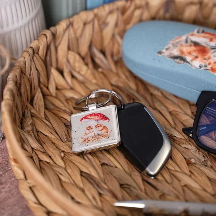 A square keychain depicting two owls sheltered under an umbrella, showcasing a whimsical design.