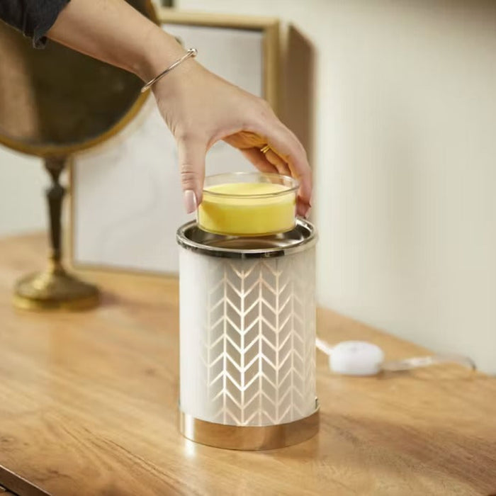Person placing a scented wax into a decorative lantern on a wooden surface.